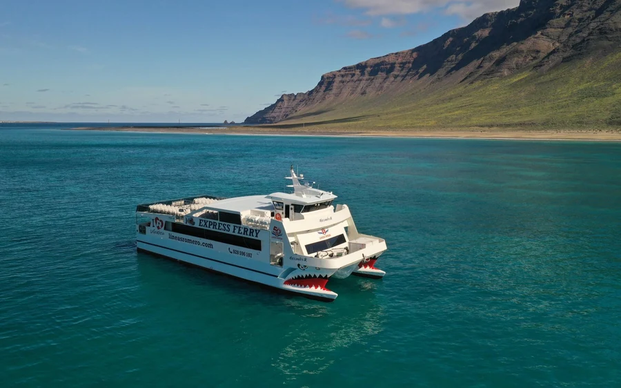 A white passenger ferry crossing turquoise water below a high green-brown cliff