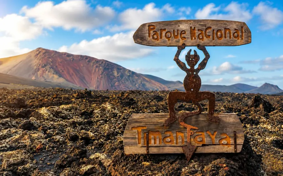 The Timanfaya sign on black lava with a red-brown volcano rising behind it