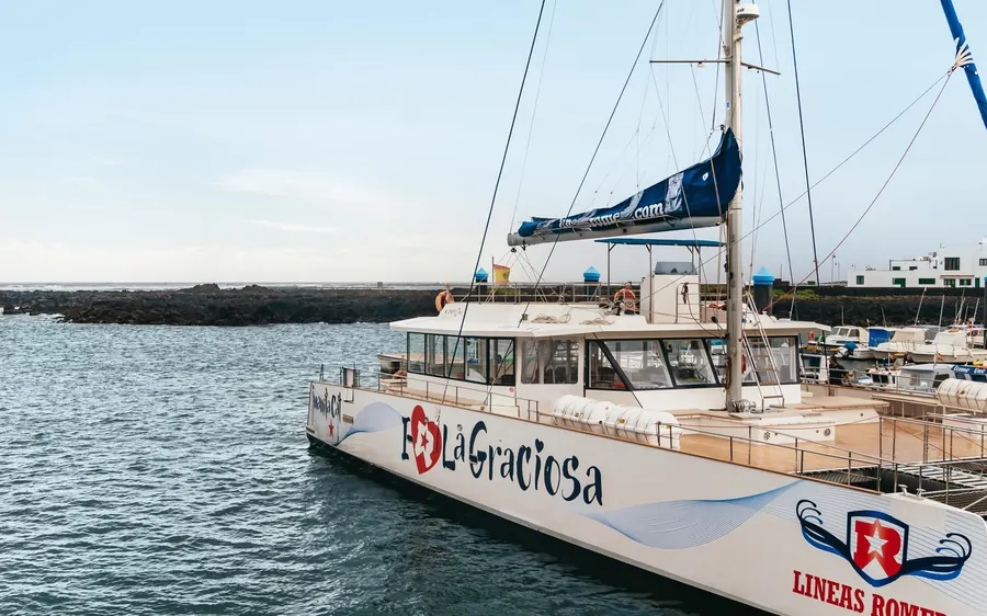 A white catamaran named La Graciosa moored beside a rocky shore