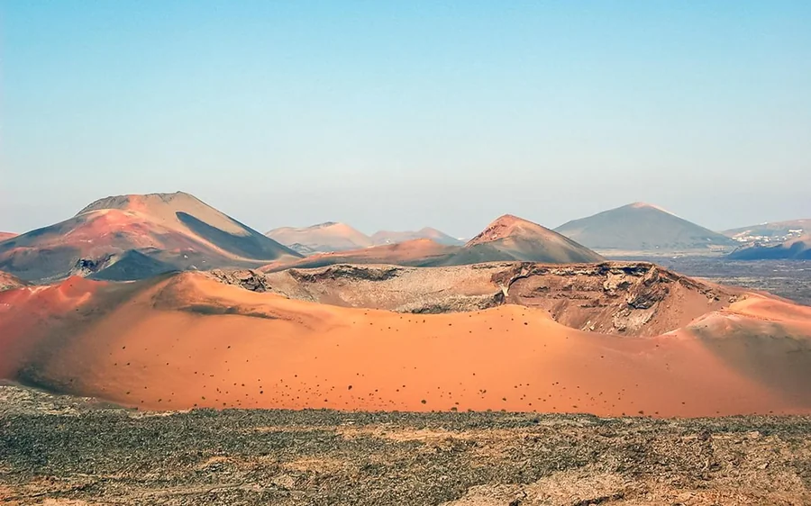A line of red and ochre volcanic cones running across a wide lava plain