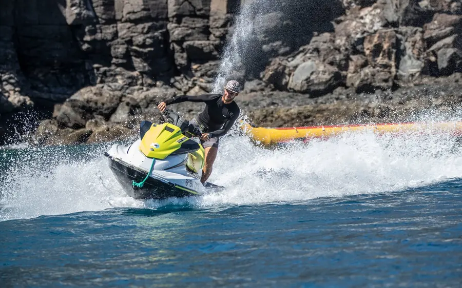 A rider on a jet ski throwing up spray below dark coastal cliffs