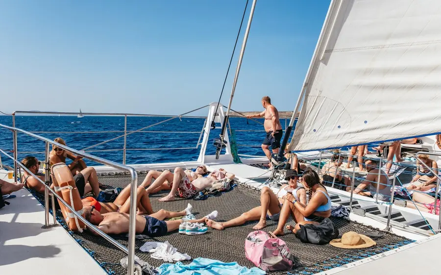 Passengers sunbathing on the deck netting of a catamaran under full sail