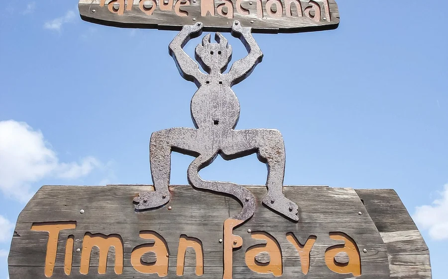 A close-up of the wooden Timanfaya park sign with its iron devil figure against the sky