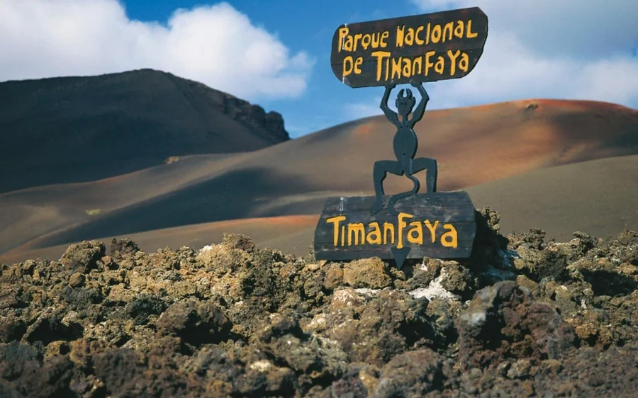 The Timanfaya park sign on a lava wall with dark and orange cones rising behind it